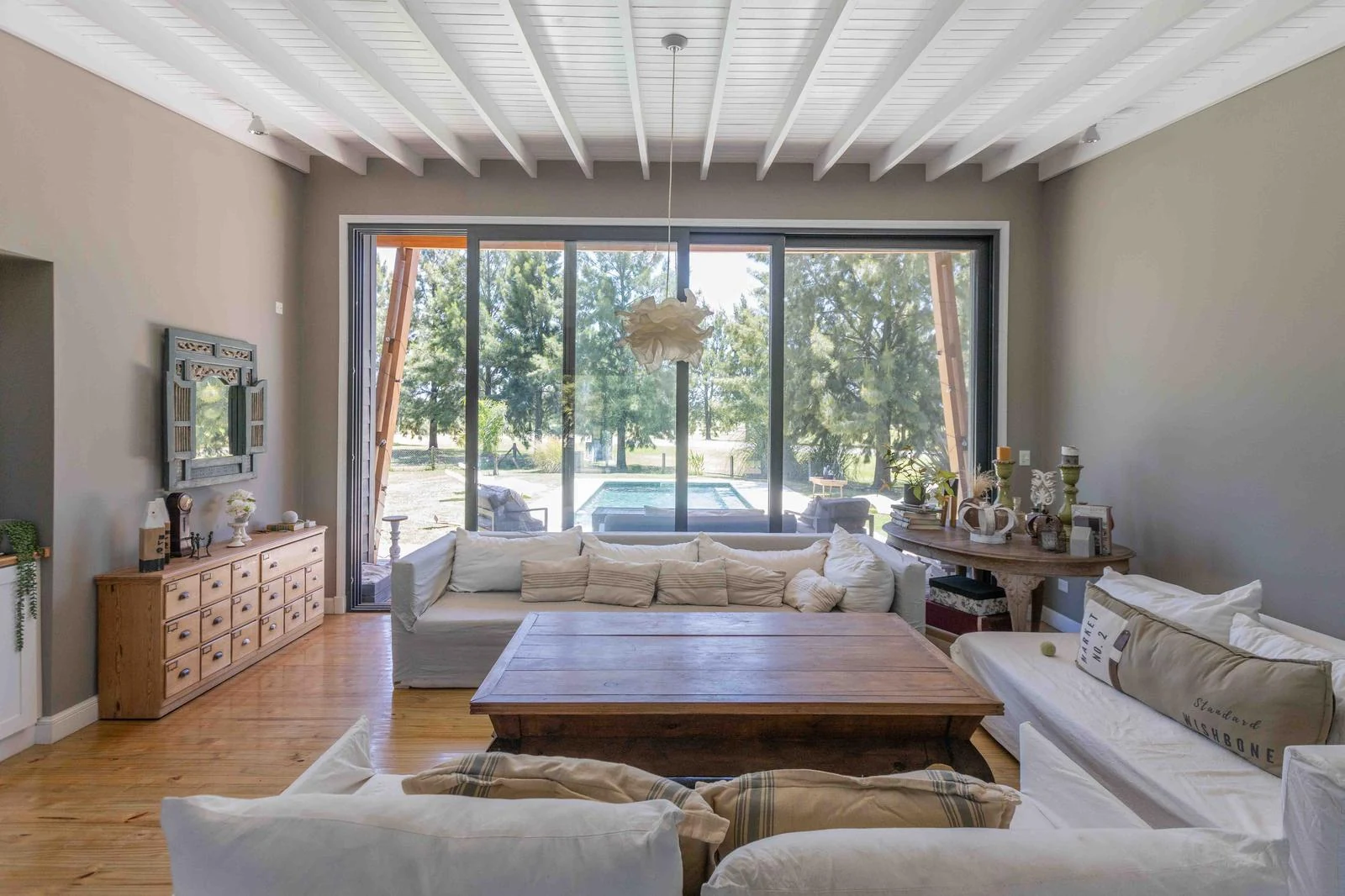 Living luminoso con techo de madera blanco y ventanales hacia el jardín