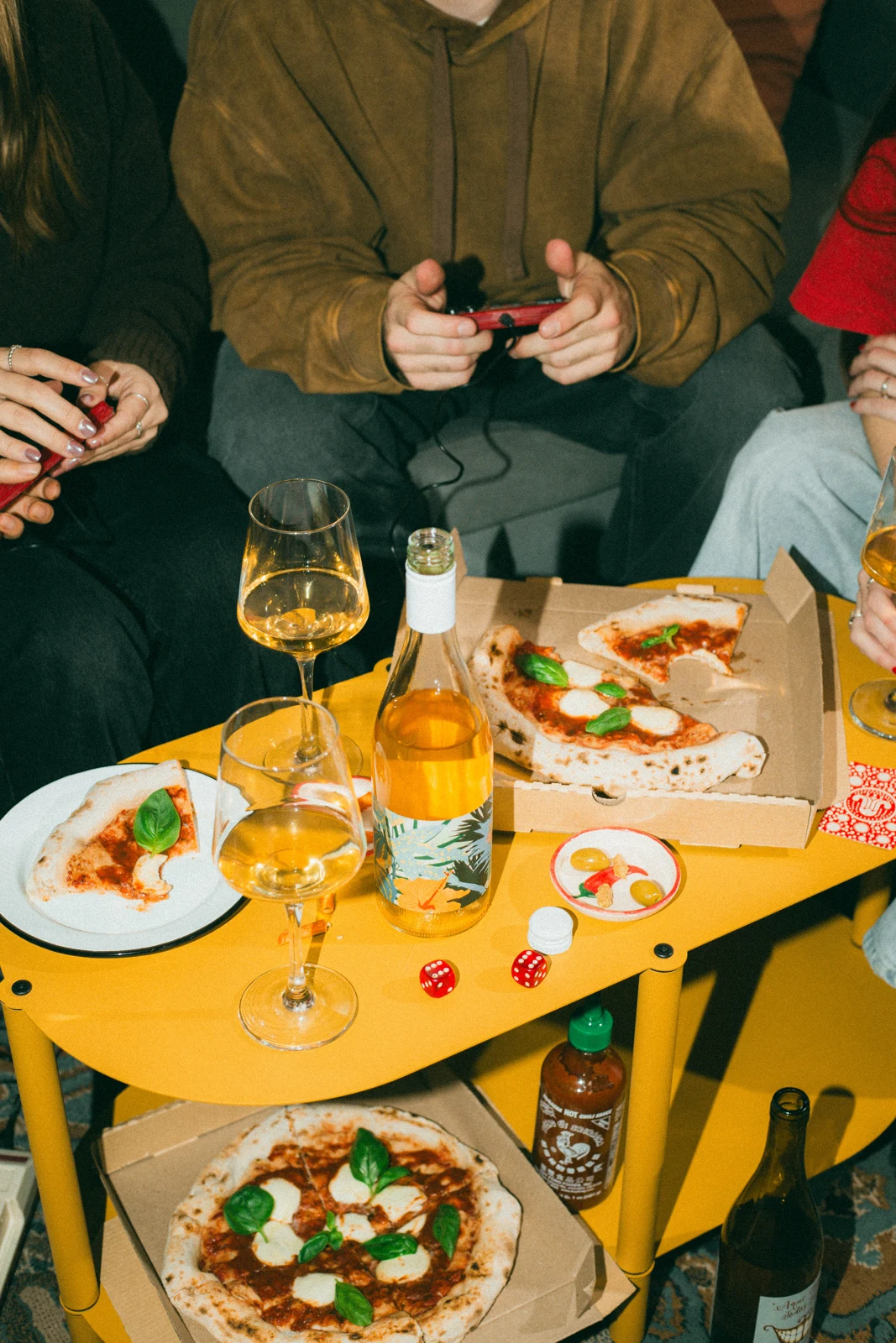 Amigos compartiendo vino, pizza y una partida alrededor de una mesa amarilla