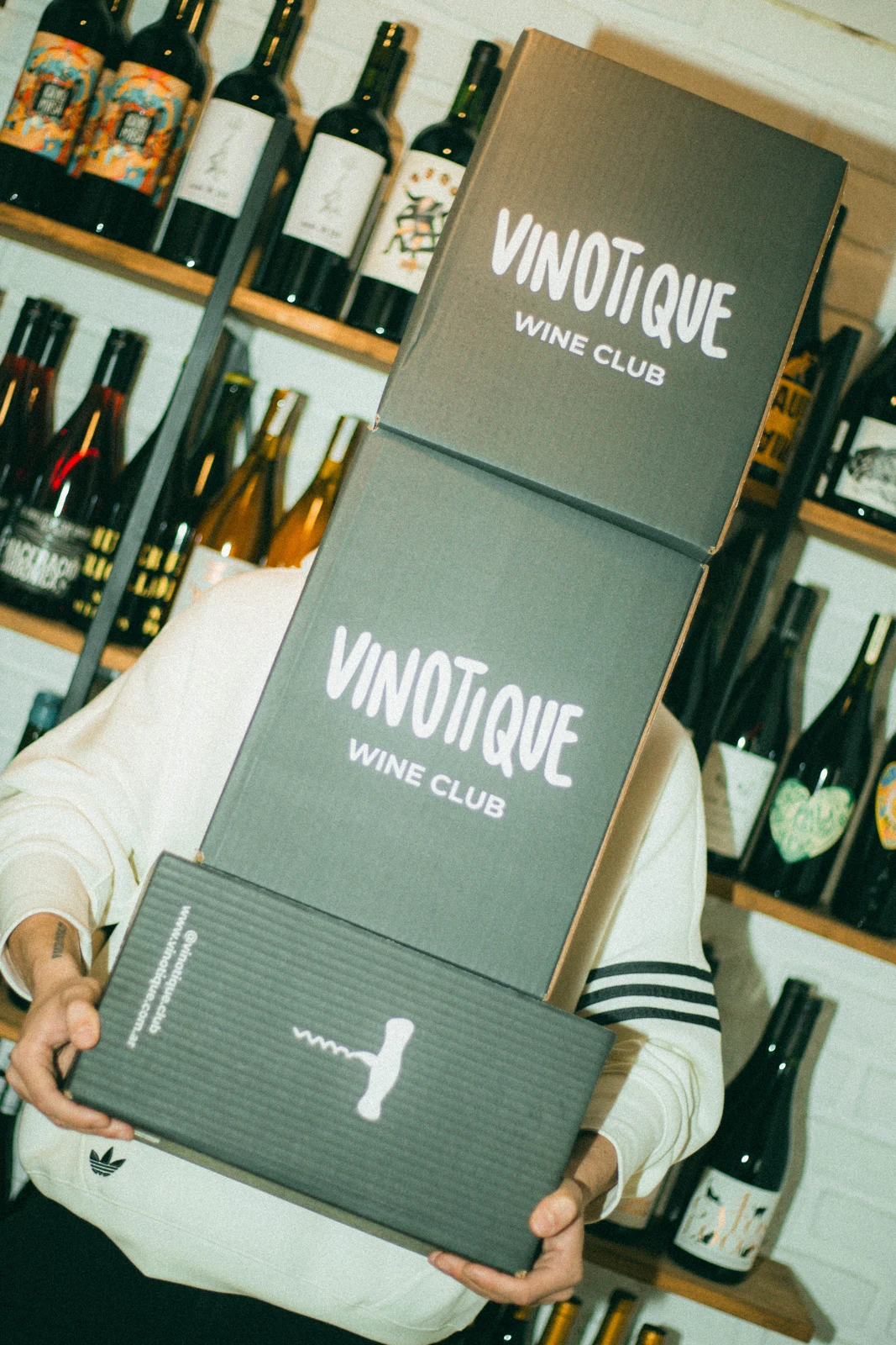 Cajas del club Vinotique frente a una estantería de vinos